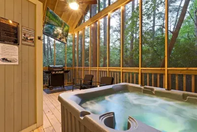 Unwind in the private hot tub surrounded by nature. Your screened-in porch includes cozy seating, a grill, and a mounted TV — perfect for relaxing rain or shine.