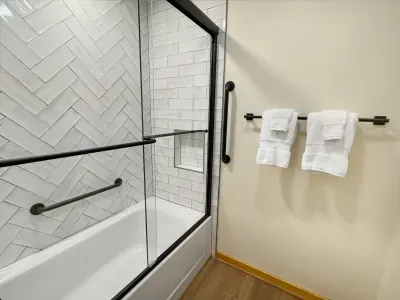Effortless elegance in every corner. 🚿 This guest bathroom features a modern glass-enclosed shower/tub combo with stylish herringbone tile and convenient safety bars. Fresh, fluffy towels await to make your stay feel like a true resort getaway.