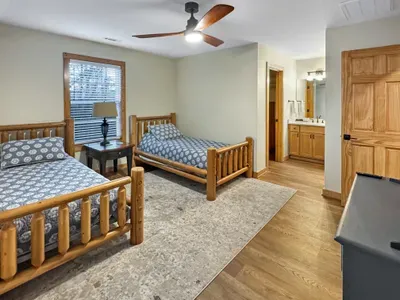 Rustic twin bedroom with ensuite vanity, ceiling fan, and wood floors