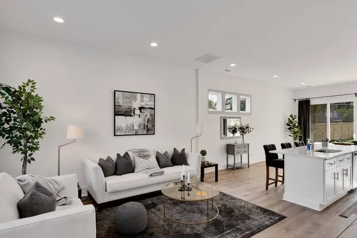 Sophisticated lounge space featuring neutral décor, plush sofas, and natural light flowing through large windows into the dining and kitchen area.