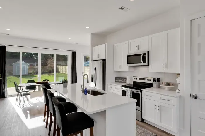 Bright, open kitchen and dining area with sleek white cabinetry, stainless appliances, and an island that flows into a sunny space with yard views