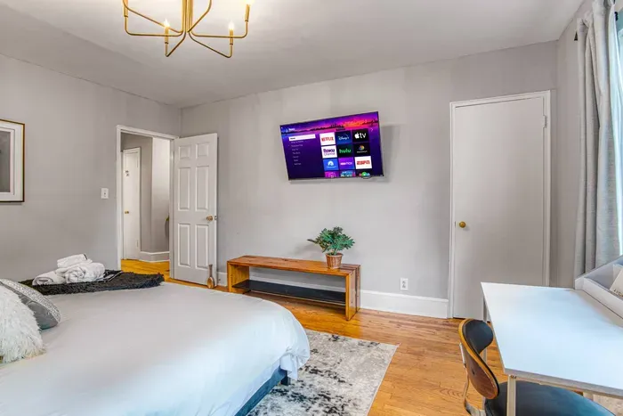 Bright, modern bedroom with a cozy bed, workspace by the window, and smart TV — designed for comfort and productivity.
