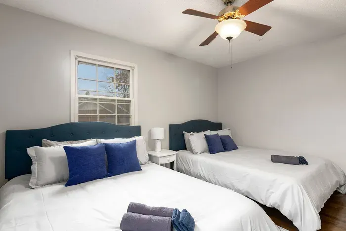 Cozy bedroom with two queen sized beds, plenty of pillows, two closets, and a nightstand with storage.