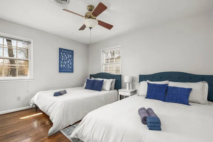 Cozy bedroom with two queen sized beds, plenty of pillows, two closets, and a nightstand with storage.