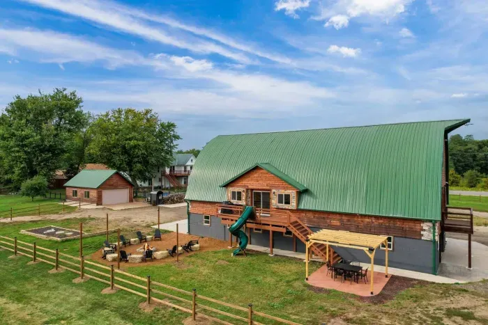 Outdoor dining area under a pergola with string lights, next to the fire pit and slide