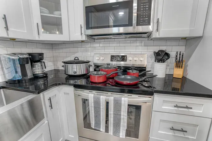 Fully equipped modern kitchen featuring stainless steel appliances, sleek black countertops, and high-quality cookware
