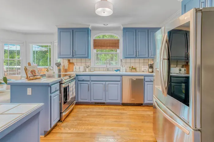 Bright kitchen with light blue cabinets, stainless steel appliances, and warm wood flooring for a cozy, modern feel.