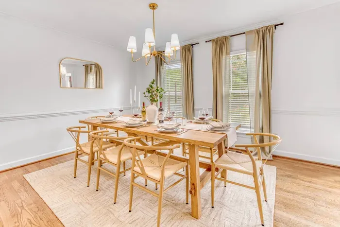 Elegant dining room good for 8 people with a wooden table set for six, gold chandelier, and soft beige curtains creating a warm, inviting atmosphere.