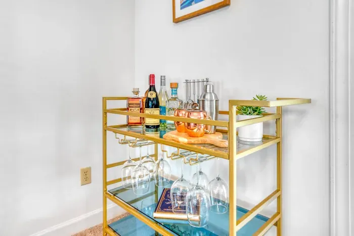 Stylish gold bar cart with glass shelves, stocked with drinks, and glassware.