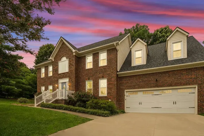 Elegant two-story brick home with white trim, a three-car garage, and a stunning sunset backdrop.