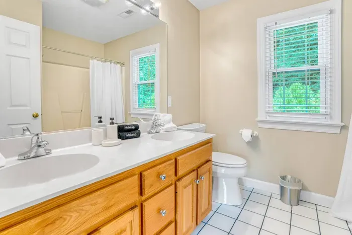 A bright full bathroom featuring a double-sink vanity, a shower-tub combo, and large windows that bring in natural light for a fresh, clean feel.