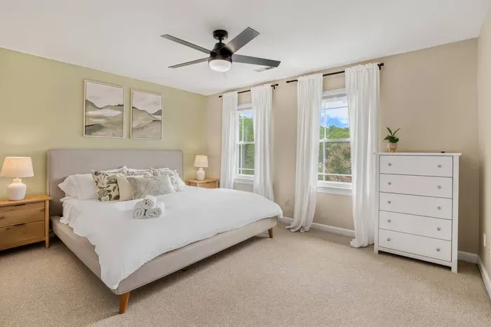 Bright and inviting bedroom that offers a plush king bed, soft neutral tones, and large windows that bring in plenty of natural light — creating a calm and airy space