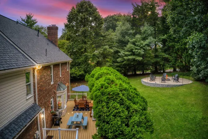 Spacious backyard retreat featuring a cozy fire pit, lush greenery, and a charming deck for outdoor dining—perfect for relaxing evenings under the sunset sky.