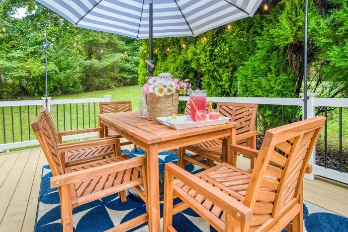 Dining setup good for 6 people featuring a wooden table and chairs under a striped umbrella