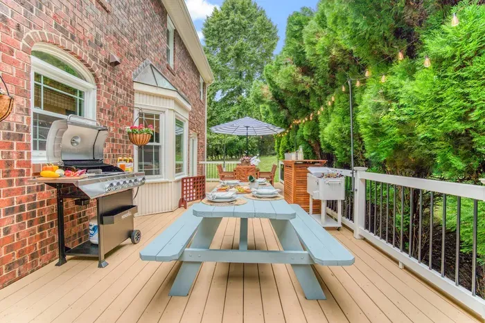 Inviting deck with a pastel picnic table, modern BBQ grill, and cozy string lights—perfect for alfresco meals surrounded by lush greenery.
