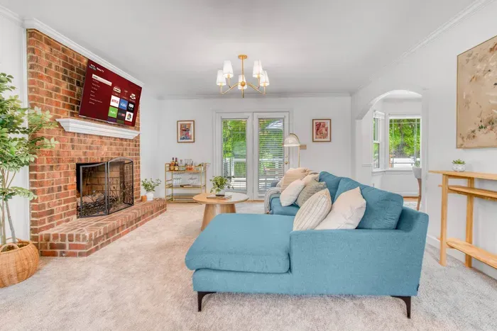 Living room featuring a spacious blue sectional sofa, a 55-inch Smart TV mounted above a classic brick fireplace, and access to the outdoor patio.