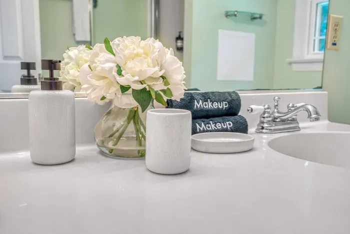 Bright bathroom vanity with fresh white flowers, sleek accessories, and neatly folded “Makeup” towels for a clean, polished touch.
