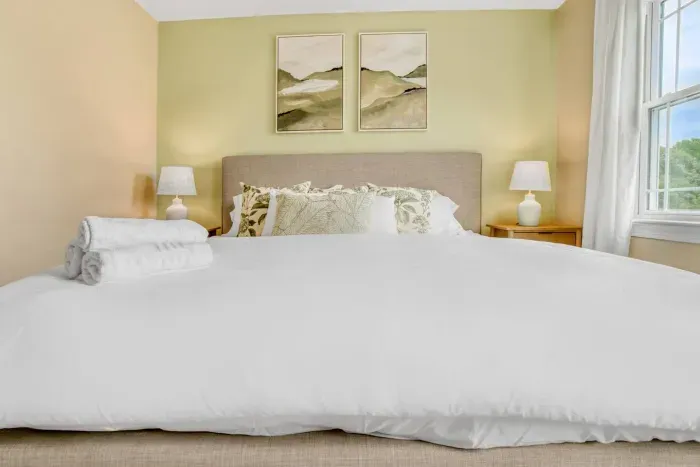 Cozy bedroom with a soft neutral palette, layered pillows, and folded towels for a fresh, inviting stay.