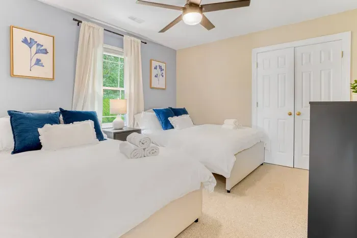 A cheerful bedroom featuring two plush full beds, soft linens, and calming blue accents — perfect for friends or family
