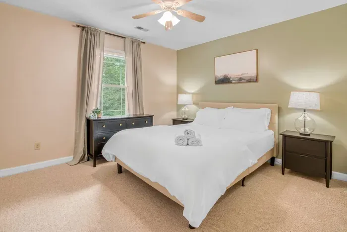 A peaceful bedroom featuring a plush queen bed, warm neutral tones, and soft lighting