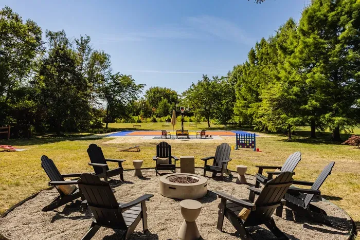 Outdoor entertainment area featuring a fire pit, set in a spacious yard with a basketball court and lawn games in the background.