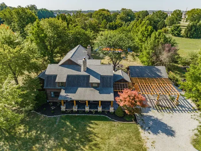 A large front porch, spacious driveway, and lush trees surrounding a peaceful property.