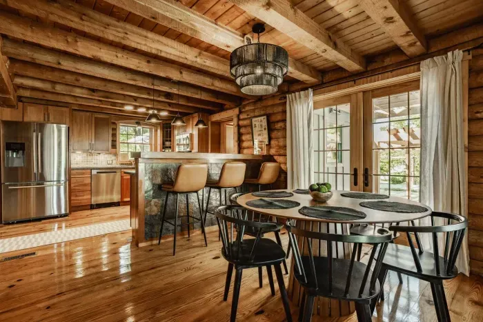 Open-concept kitchen and dining space with rustic wood beams, modern finishes, and bright natural light from large French doors.