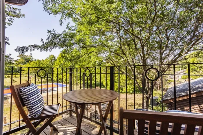 A balcony retreat with a wooden bistro set, framed by elegant wrought-iron railings and shaded by lush trees—perfect for morning coffee or quiet outdoor moments.
