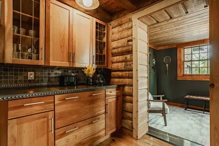 Kitchen nook with warm wood cabinetry, glass-front details, and a smooth transition into a bright adjoining room.
