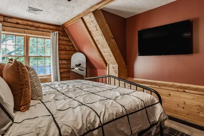 Charming cabin-style bedroom with natural wood finishes, a comfy bed, and a flat-screen TV.