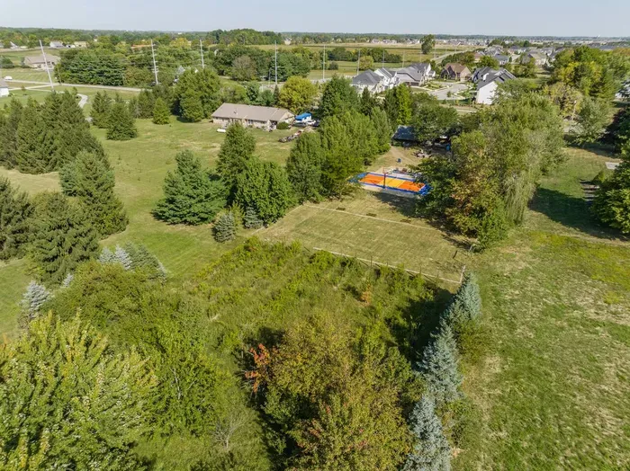 Spacious property surrounded by trees with open green areas, a sports court, and plenty of room to relax or play outdoors.