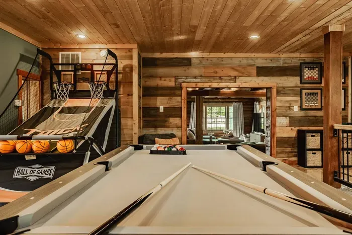 Rustic game loft featuring a pool table, basketball arcade game, and cozy wood-paneled design.