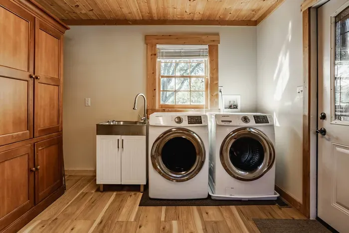 Fully functional laundry room featuring a washer and dryer set, utility sink, and large wooden cabinet.