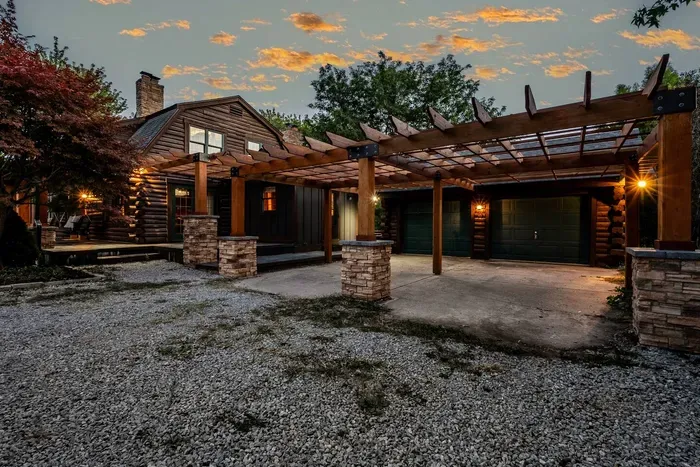 Spacious covered driveway and garage area featuring a beautiful wooden pergola and stone pillars.