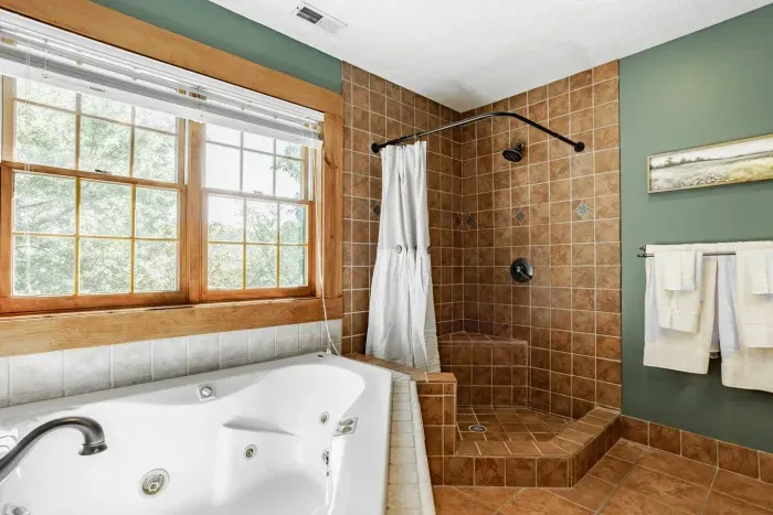 Spacious bathroom featuring a relaxing jetted tub, walk-in tiled shower, and large window for natural light.