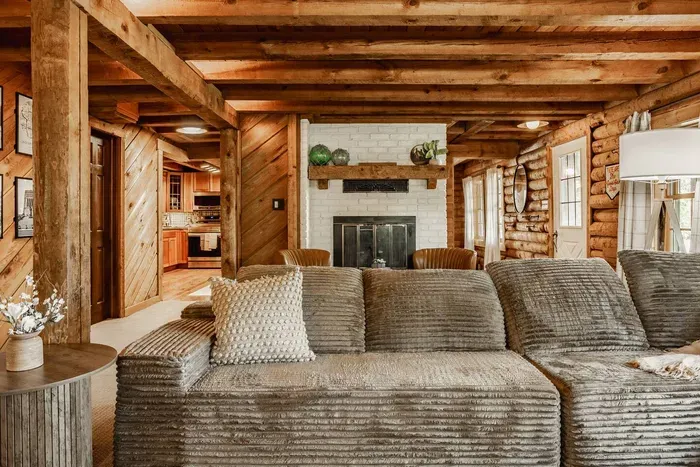 Warm and inviting log cabin living room featuring a plush sectional sofa, rustic wood beams, and a brick fireplace—perfect for relaxing after a day outdoors.