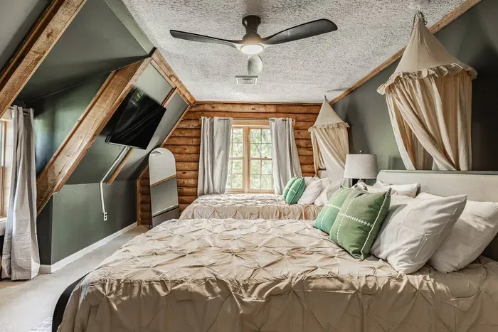 Loft bedroom featuring two stylish beds, unique sloped ceilings, and a warm cabin feel — a perfect blend of comfort and charm for a restful stay.