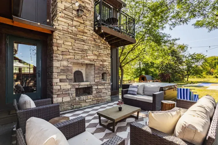 An outdoor living area showcasing a stone fireplace as the focal point, surrounded by cushioned wicker sofas and armchairs.