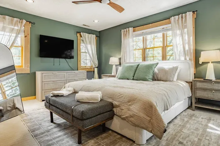 Elegant, soft neutral toned bedroom with a comfortable king bed, soft lighting, and large windows creating a calm, airy atmosphere.