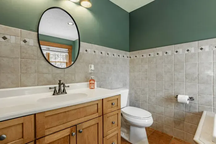 Featuring a wooden vanity with a white countertop, an oval mirror, and classic tiled walls. 