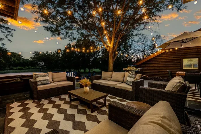 Outdoor lounge perfect for evening gatherings with warm string lights, comfortable wicker seating, and a large tree centerpiece.