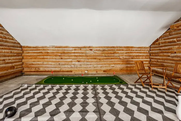 Game loft with rustic log walls, featuring a mini putting green, bowling set, and seating area—perfect for indoor fun.