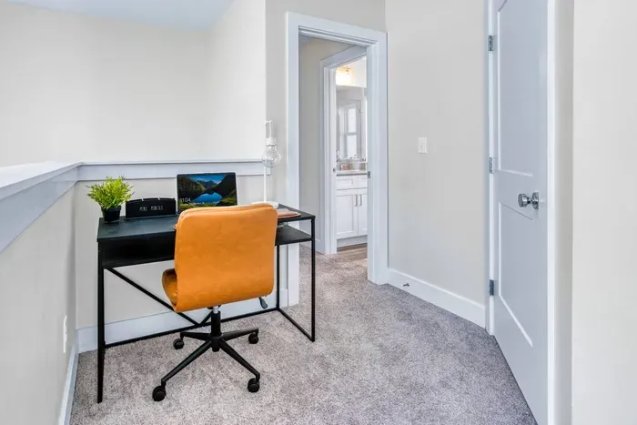 Featuring a sleek black desk, warm leather chair, and soft carpeted flooring