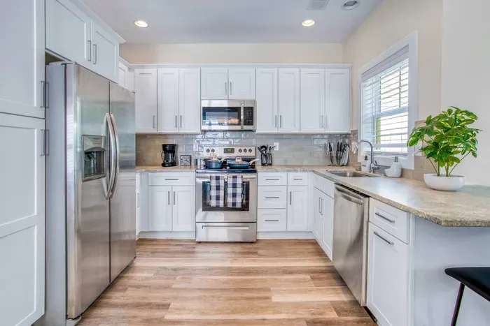 Kitchen that blends form and function, featuring modern appliances, sleek white cabinetry, and warm wood floors for a clean, airy feel.