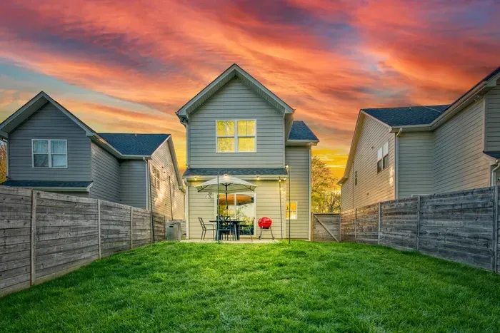 Inviting backyard patio with string lights, outdoor dining, and a grill — perfect for relaxing or entertaining under the sunset.