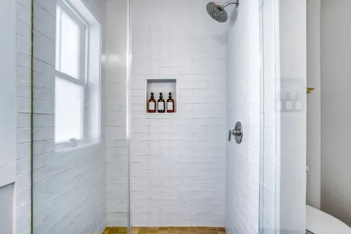 A sleek walk-in shower featuring white subway tiles, built-in shelving, and a rainfall showerhead
