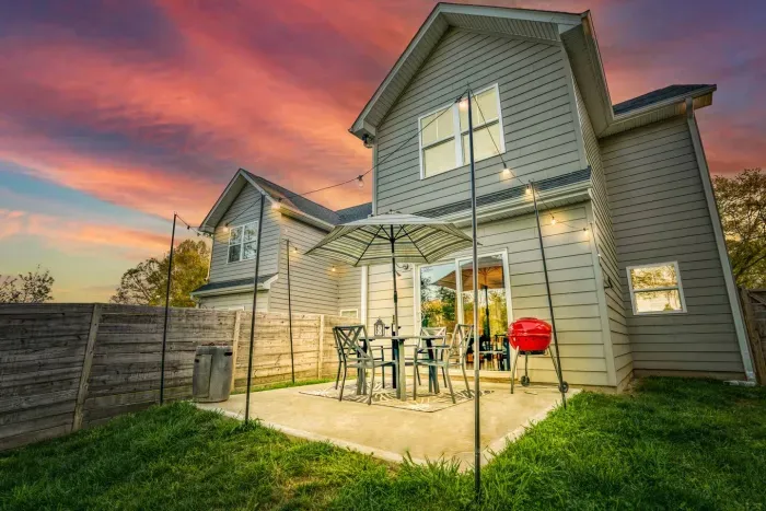 Inviting backyard patio with string lights, outdoor dining, and a grill — perfect for relaxing or entertaining under the sunset.