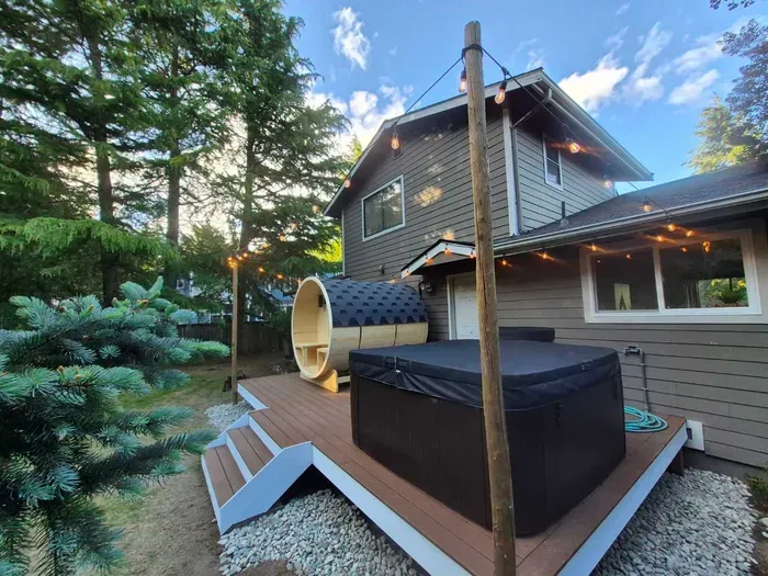 Hot tub and barrel sauna below the string lights facing the golf course and woods