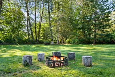 The lawn-side fire pit is surrounded by rustic seats and trees. Use only when permitted; bring your own firewood.
