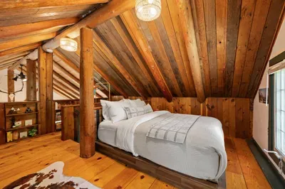 The loft sleeping area offers a comfortable bed beneath the cabin’s sloped wood ceiling.